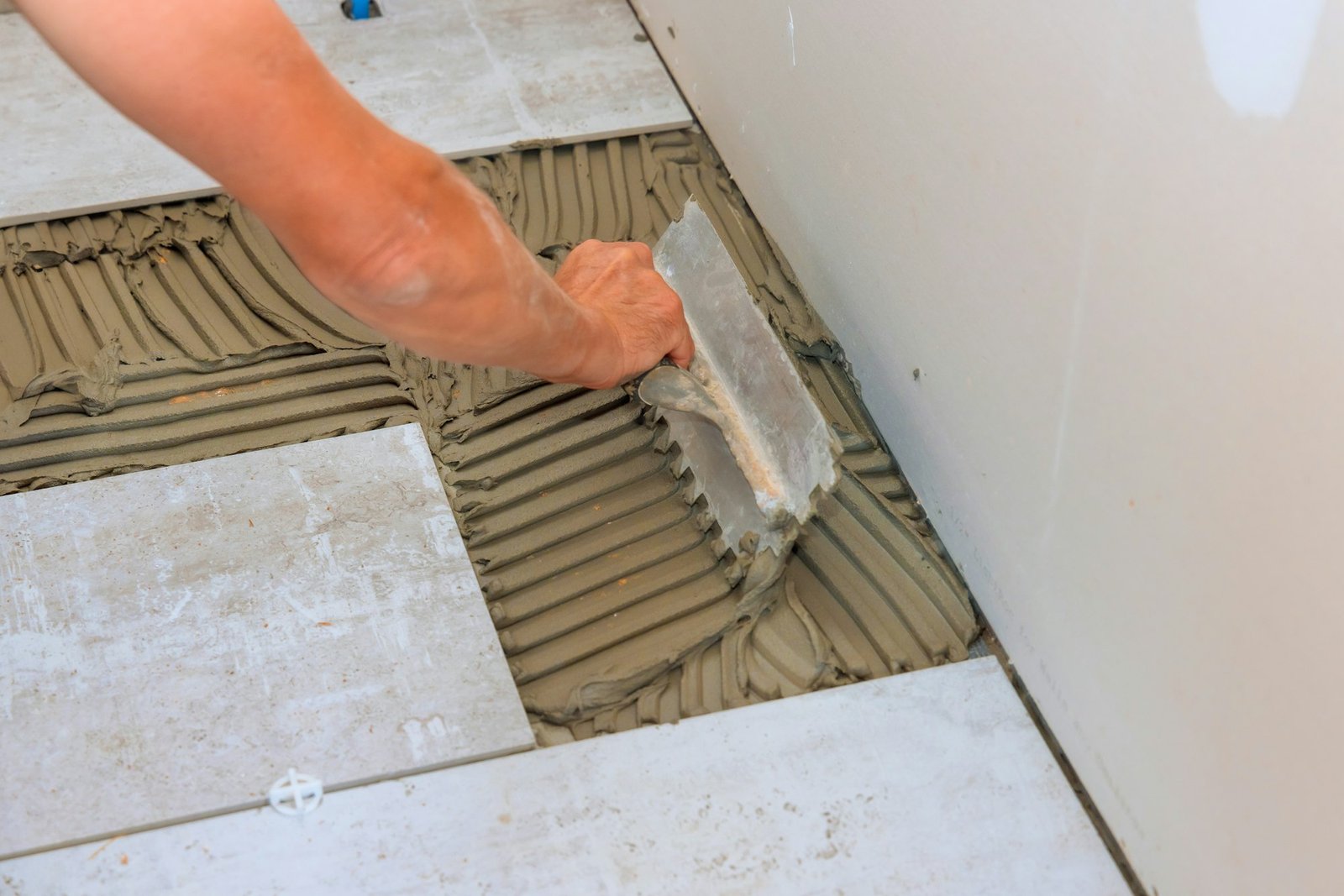 Troweling adhesive onto a concrete floor in preparation for laying floor tile.