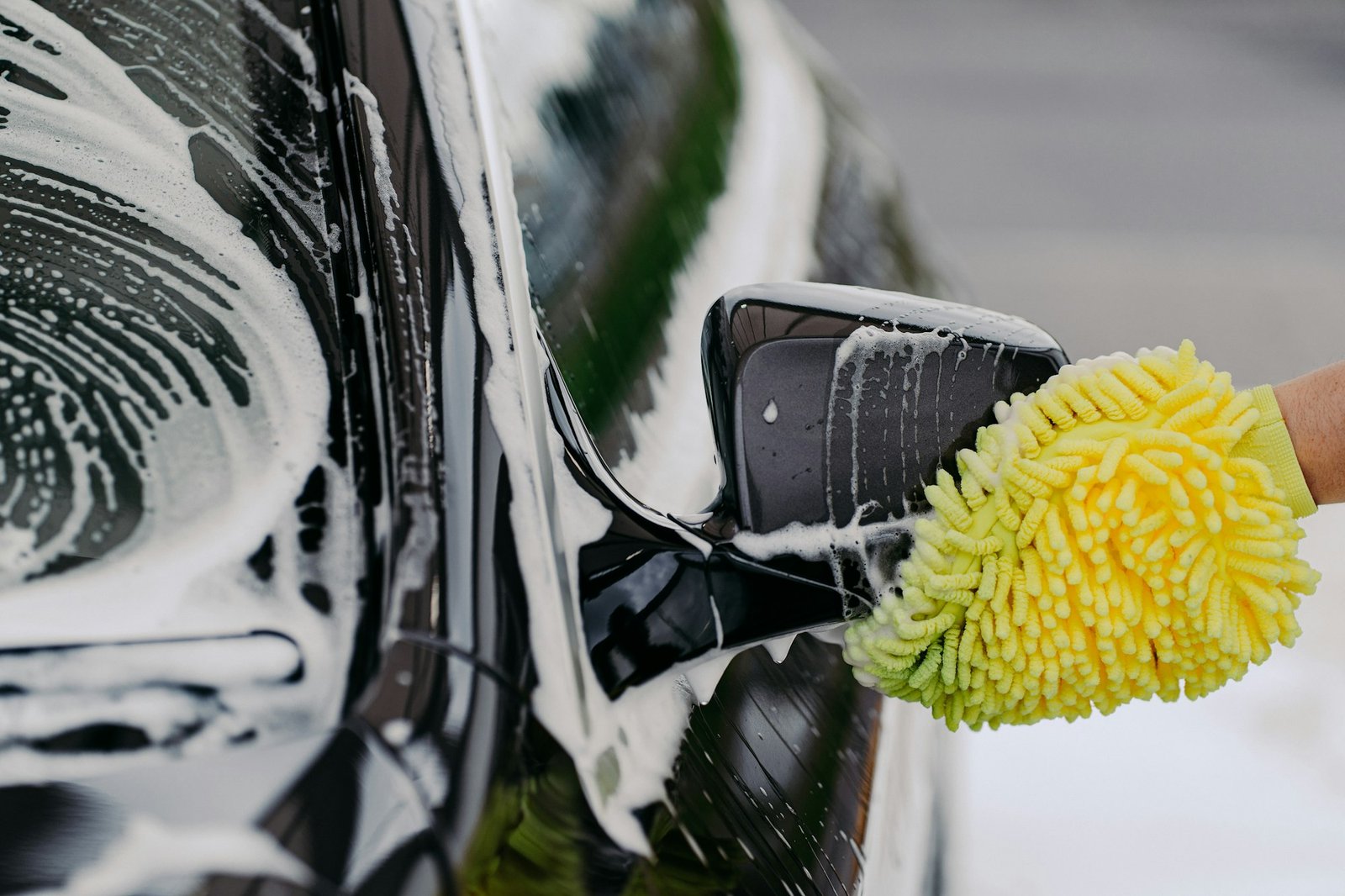 Unrecognizable man washes black car with cloth or rag mitten, uses special detergent