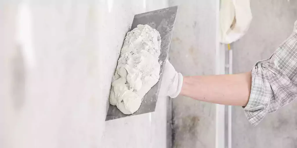 The worker uses a flat trowel to apply white cement slurry onto the cement façade wall.