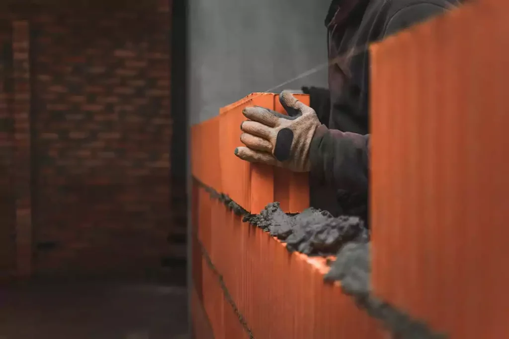 Builder laying a large brick block on the mortar creating a wall