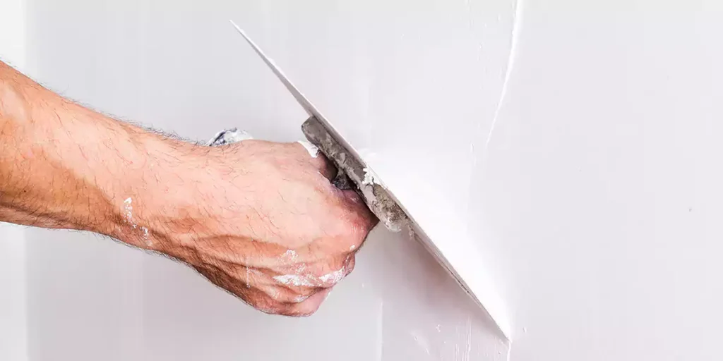 A hand using a trowel to smooth white cement plaster on the wall.