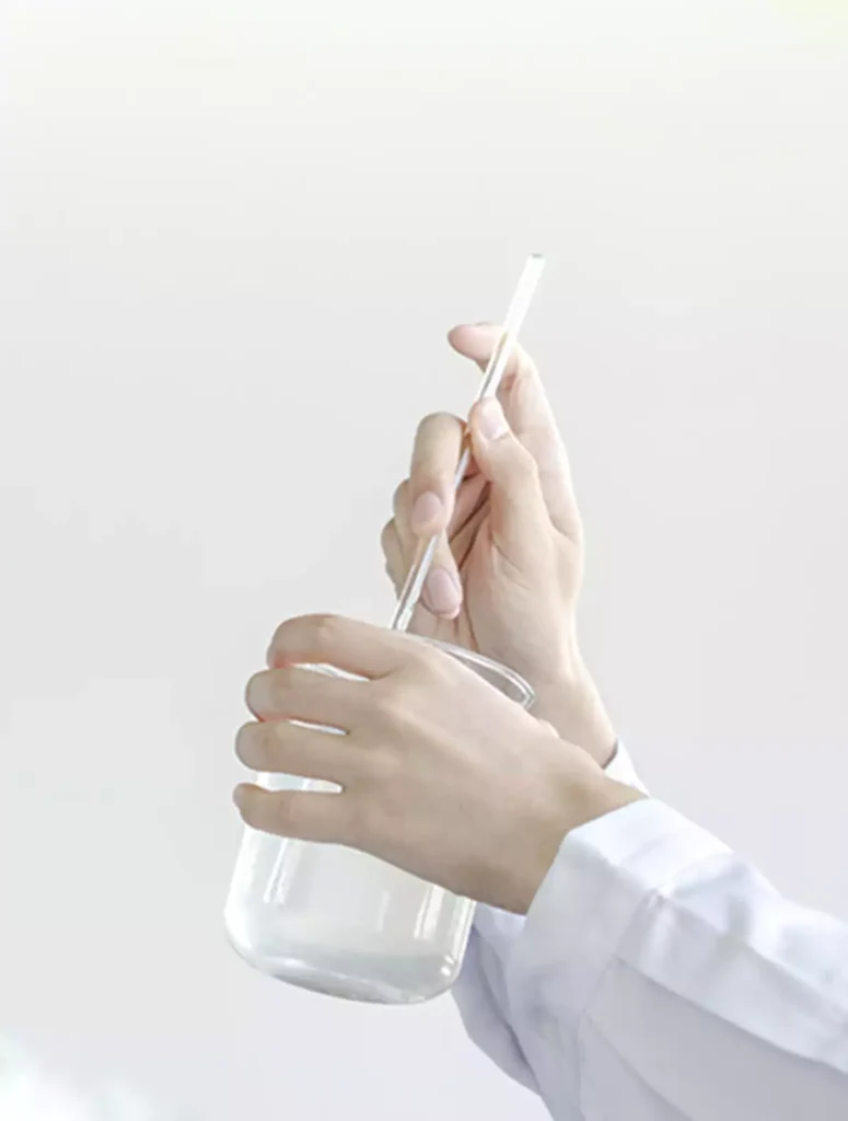 A lab technician in a white lab coat is stirring a solution in a glass beaker with a glass rod.